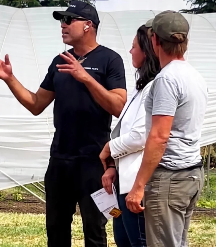 People talking together beside protected growing structures on a farm